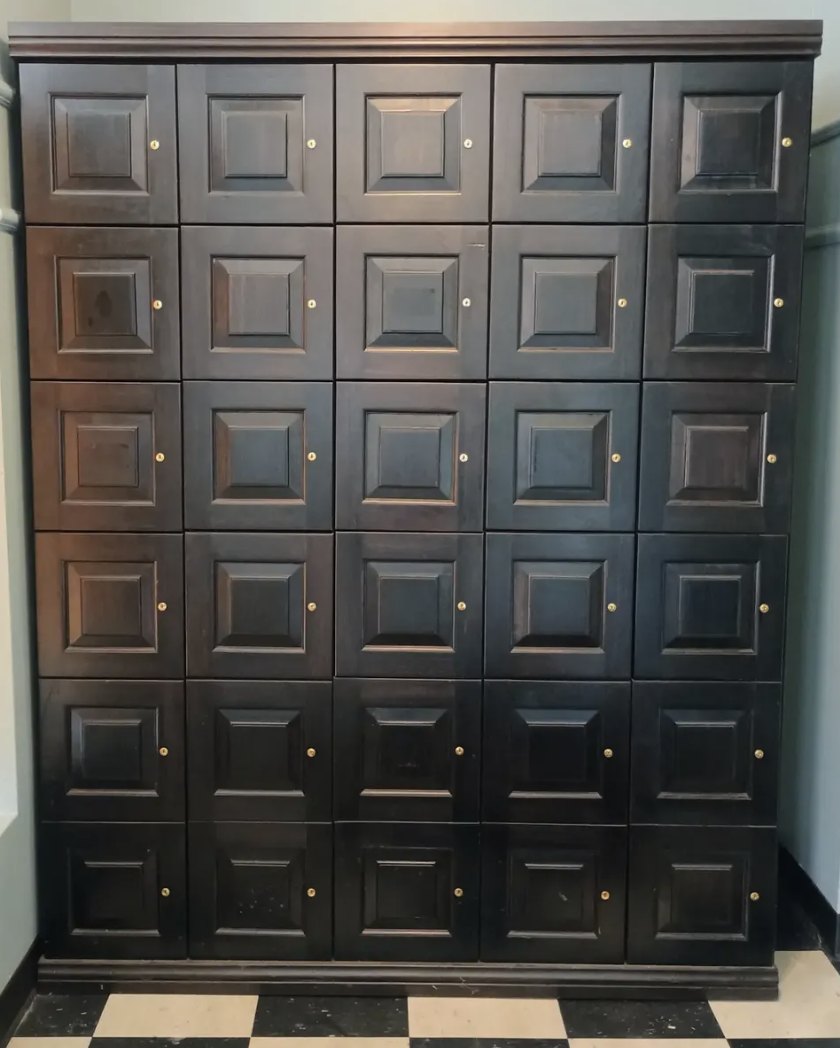 Wall of dark wood private cigar lockers with brass locks above a black and white checkered floor at Ember Premium Cigar Lounge