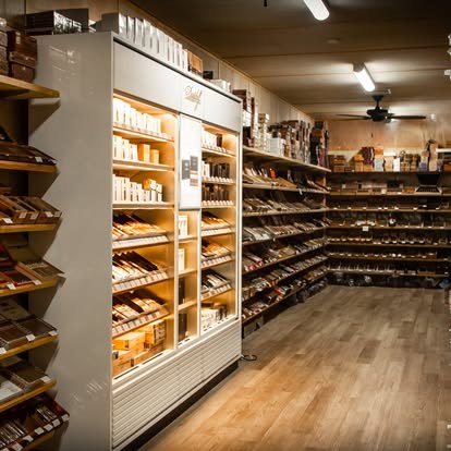 Walk-in humidor at Fogue & Bates with wooden shelves of cigar boxes along the walls and a lit Davidoff display cabinet