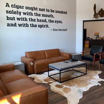 Lounge at Fogue & Bates with tan leather sofas, a concrete coffee table on a cowhide rug, and a Zino Davidoff quote painted on the wall
